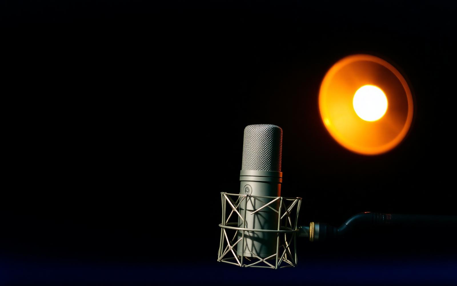 A studio condenser microphone lit by a single warm lamp